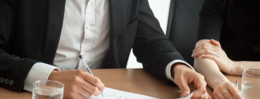 Satisfied smiling businessman in suit signing contract at meetin